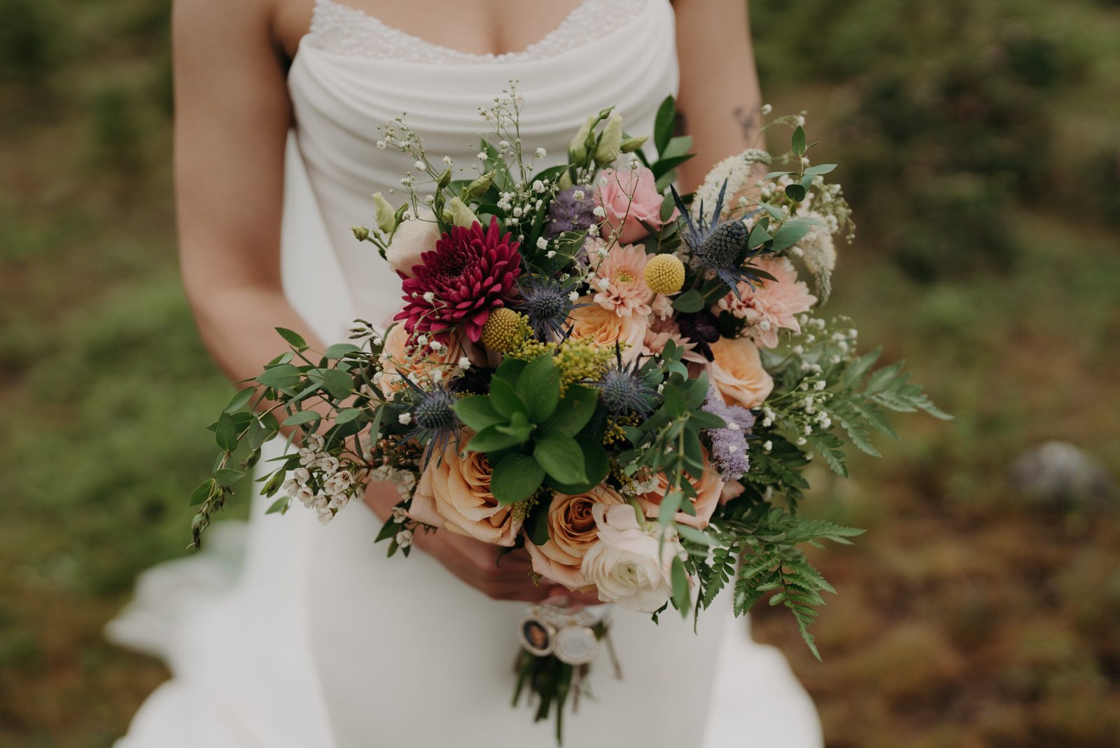 A direct front view close-up of a diverse wedding bouquet with multiple flower types, including large purple dahlias and small peach roses.