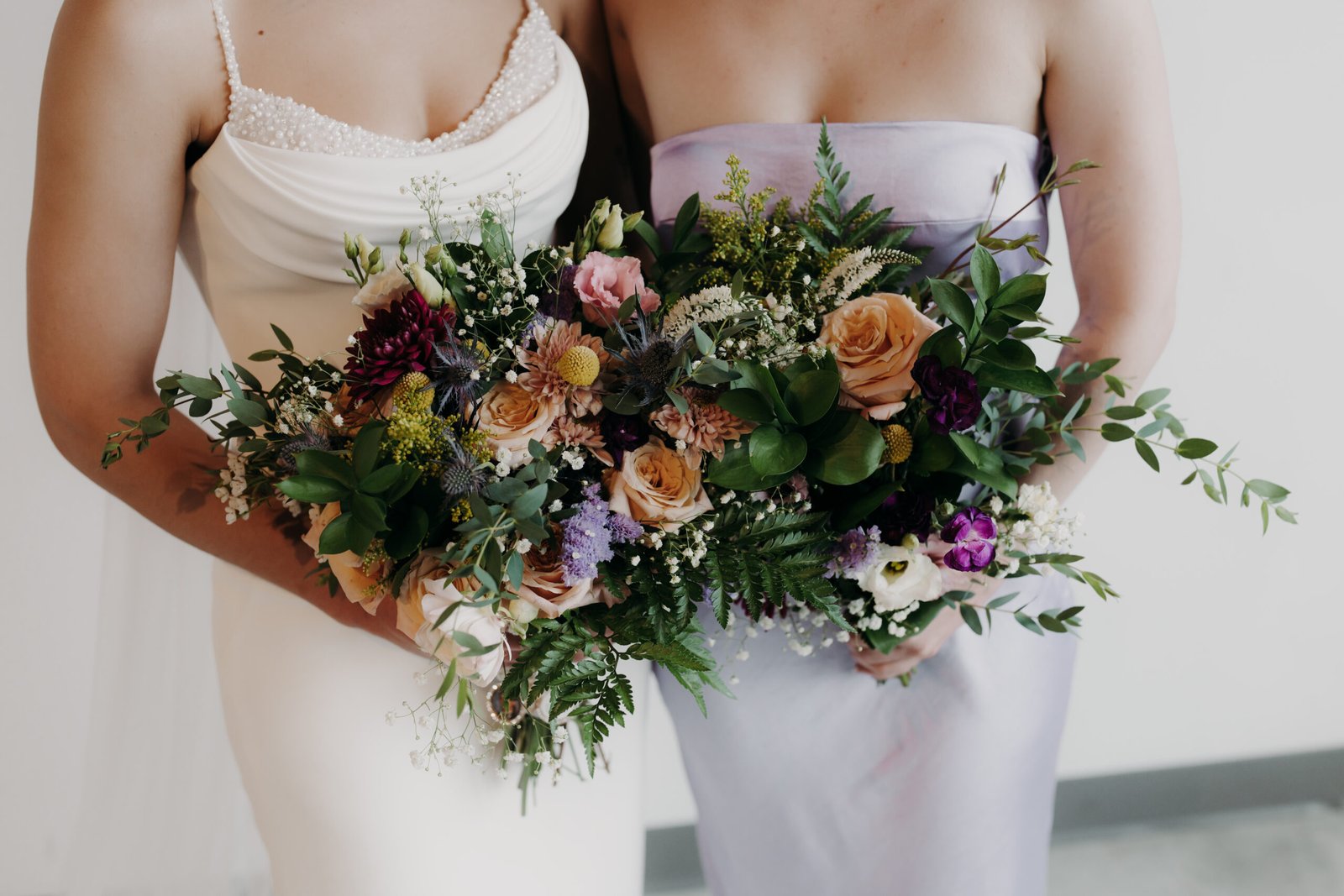 Close-up of a rustic bridal bouquet with peach roses, blue thistles, and burgundy dahlias.